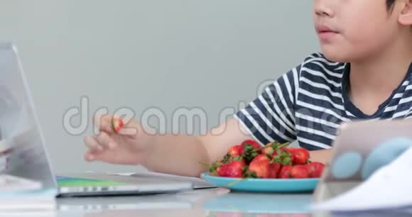小亚洲男孩在家吃草莓和使用笔记本视频的预览图