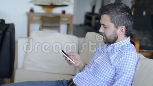 男人坐在沙发上用智能手机和智能手表视频的预览图