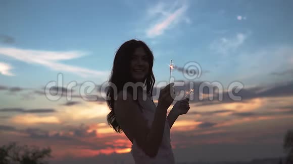 在日落时幸福女孩的手中闪烁着天空一个穿着鸡尾酒礼服的漂亮女孩的肖像慢慢慢慢视频的预览图