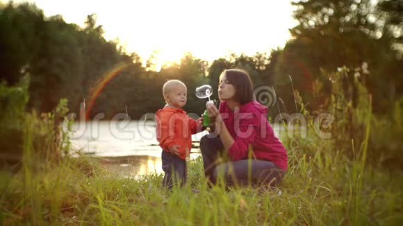 漂亮的年轻妈妈和她的小儿子一起快乐地在日落时分吹泡泡视频的预览图