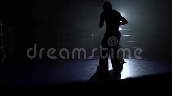 一个戴着头盔和拳击手套的女孩在黑暗中在拳击场上打的家伙剪影视频的预览图