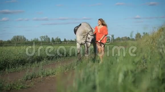 一位美丽迷人的金发女人带着马在田野里散步视频的预览图