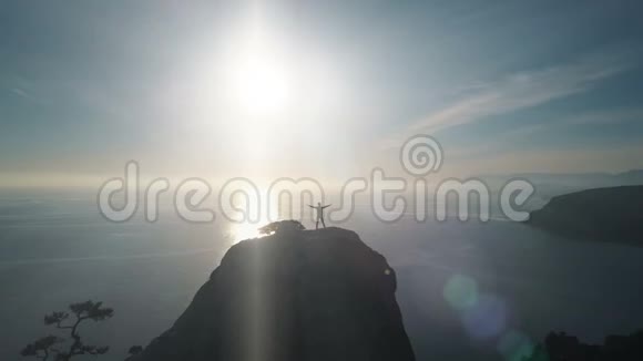 一位年轻女子站在一座面向大海的山顶上的空中轮廓在美丽的山顶上的女士视频的预览图