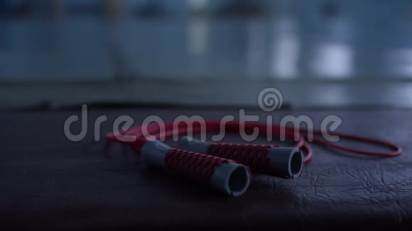 黑色健身房地板上有黑色手柄的红色跳绳特写视频的预览图