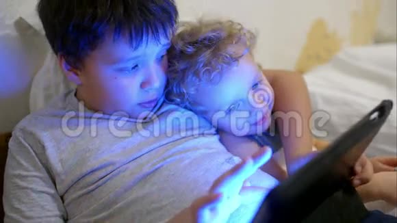 两个男孩躺在床上带触摸垫一个玩游戏视频的预览图
