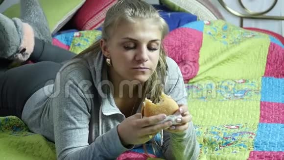 满意的女人在她房间的床上吃快餐汉堡很垃圾的食物慢动作视频的预览图