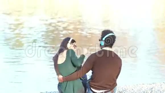 一对情侣坐在湖边用耳机听音乐视频的预览图