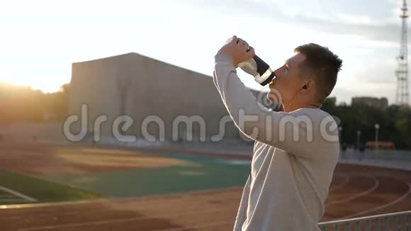 戴着naseball帽子的疲惫的运动员在体育场跑道上喝着瓶子里的水视频的预览图