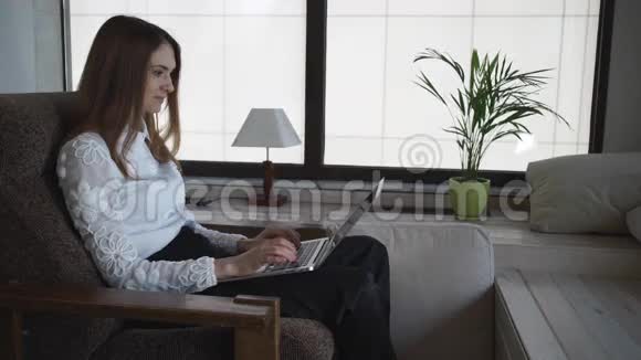 家庭大窗户附近的笔记本电脑上的女性类型视频的预览图