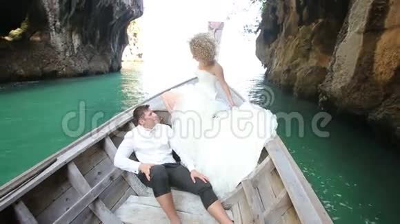 金发新娘和新郎乘长尾船在悬崖上漂浮视频的预览图