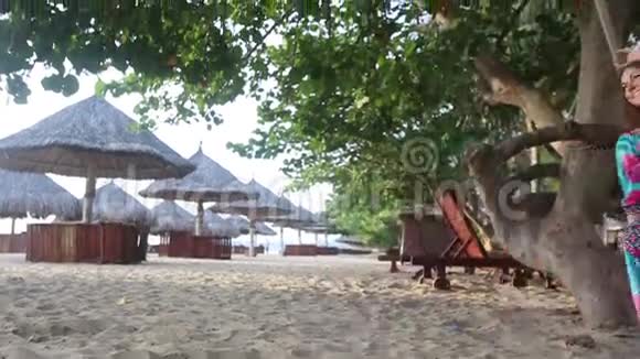 穿着长裙的女孩在靠近雨伞的海滩上摇摆视频的预览图