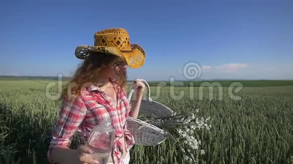 年轻的女人带着花篮和一瓶水走着背景上有蓝天的麦田慢慢慢慢视频的预览图