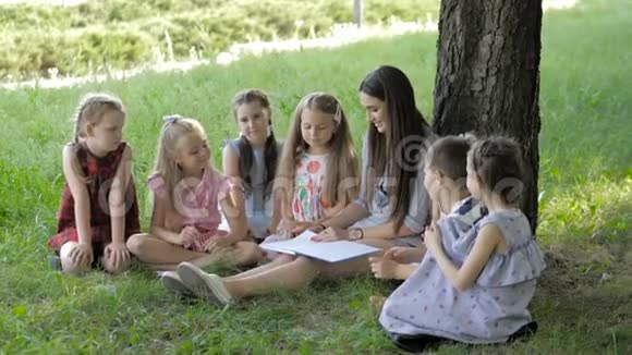 儿童和教育年轻妇女在工作中作为教育者向公园的男孩和女孩读书视频的预览图
