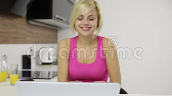 坐在餐桌厨房里的年轻女人在打手提电脑视频的预览图