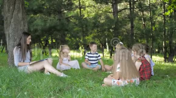儿童和教育年轻妇女在工作中作为教育者向公园的男孩和女孩读书视频的预览图