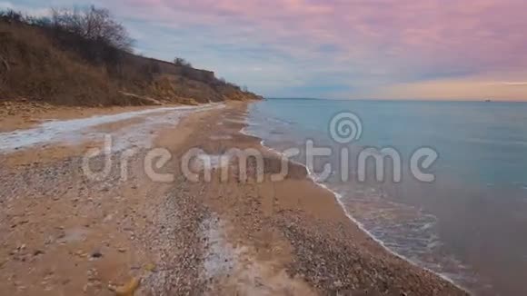 在美丽的粉红色日落期间史诗般的飞行无人机飞越冬季海滩4K视频的预览图