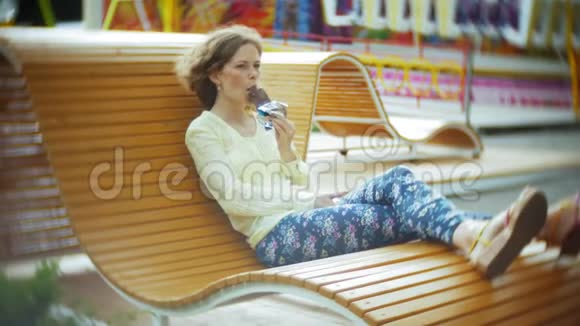 美丽的女人吃冰淇淋在公园里的木凳上工作视频的预览图