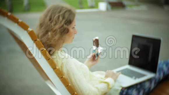 美丽的女人吃冰淇淋在公园里的木凳上工作视频的预览图
