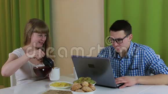 年轻人坐着看着笔记本电脑他工作很忙不关心他的妻子她提供早餐视频的预览图