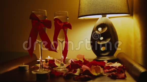浪漫的室内两只带红色丝带的眼镜床上的玫瑰花瓣视频的预览图
