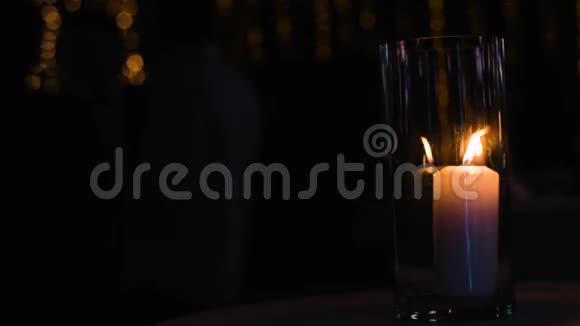大白蜡烛站在玻璃杯下的桌子上而有人站在杯子里的背景上视频的预览图