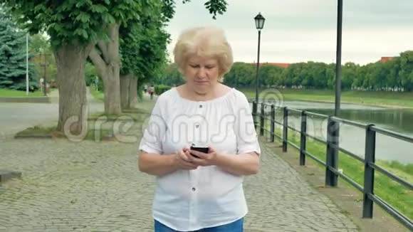 老年妇女沿着海滨散步使用智能手机河流的背景视频的预览图