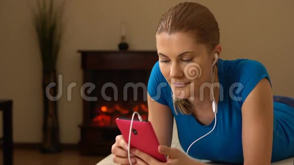 美丽迷人的年轻女人一部智能手机躺在沙发上听音乐视频的预览图