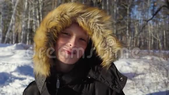 一个十几岁男孩的特写男孩微笑流露出情感阳光明媚的冬天晚上在森林里视频的预览图