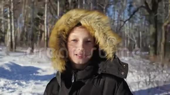 一个十几岁男孩的特写男孩微笑流露出情感阳光明媚的冬天晚上在森林里视频的预览图
