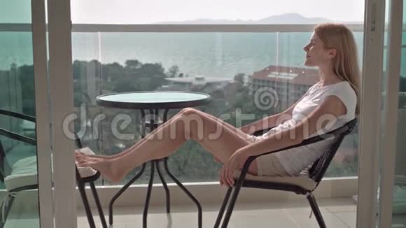 美丽迷人的女人坐在阳台的椅子上放松享受风景青绿色的海树视频的预览图
