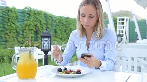 漂亮的女人用智能手机在咖啡馆里吃沙拉视频的预览图