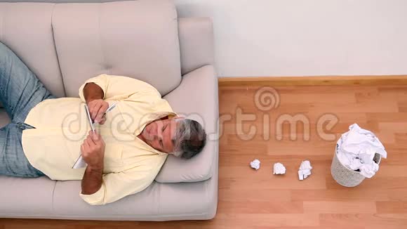 成熟的男人躺在沙发上写着想法把它们扔出去视频的预览图