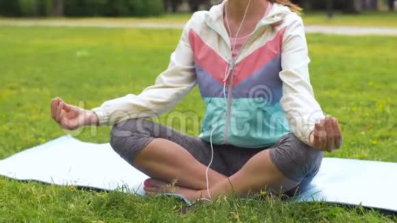 戴着耳机的女人在公园打坐视频的预览图