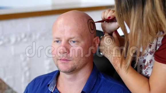 一个女孩一个大师一个艺术家一个纹身在头皮上画指甲花一个秃顶的白种人一个蓝色的男人视频的预览图
