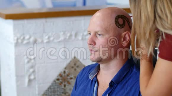 一个女孩一个大师一个艺术家一个纹身在头皮上画指甲花一个秃顶的白种人一个蓝色的男人视频的预览图