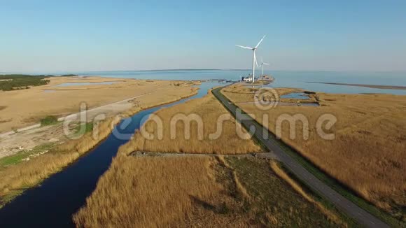 4K鸟瞰蓝色河流田野道路和转弯风力涡轮机靠近大海视频的预览图