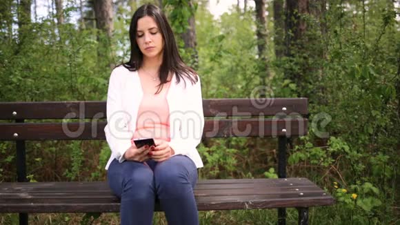 迷人的微笑的年轻女人带着智能手机在公园里滑动滑块视频的预览图