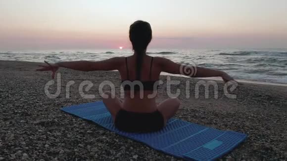 美丽的年轻女子在海滩上做瑜伽同时观看日落视频的预览图