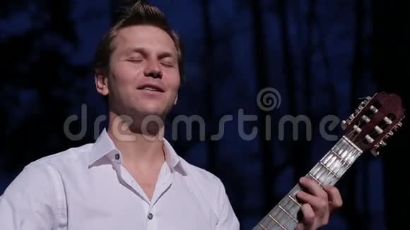 一个穿着白色衬衫的可爱的年轻人弹吉他唱小夜曲视频的预览图