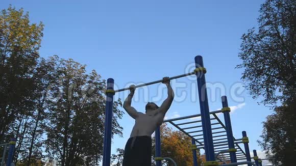 强壮的肌肉男在公园里做肌肉锻炼年轻运动员在户外水平杆上做下巴练习健身视频的预览图