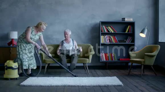 一位老年妇女用吸尘器清理地板一位老年男子正在看报纸视频的预览图