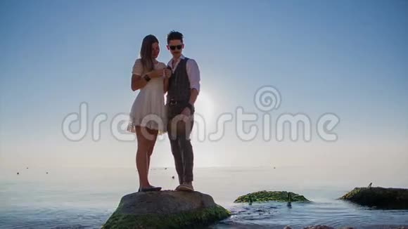 日落时分一对夫妇站在水中的岩石上视频的预览图