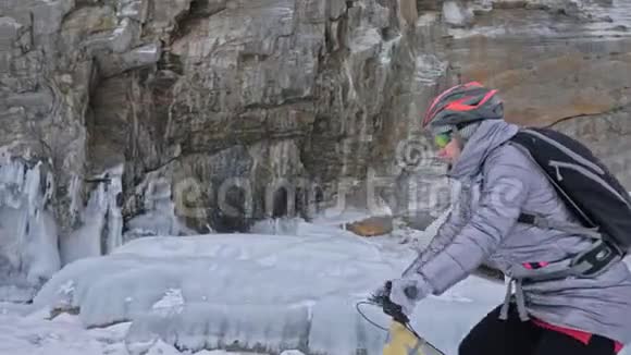 女人正在冰窟附近骑自行车有冰洞和冰柱的岩石非常美丽女孩穿着视频的预览图