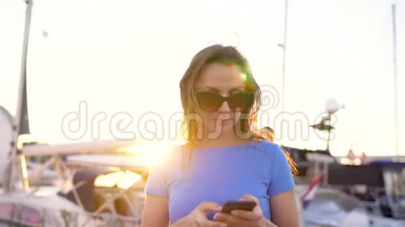日落时分戴着墨镜的女人在码头上行走时带着很多游艇和船只靠近靠近视频的预览图