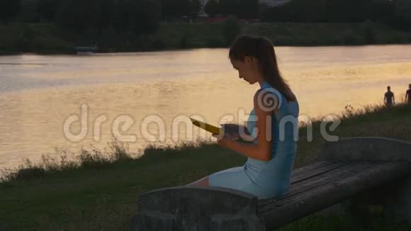 日落时分女人在长凳上看电子图书视频的预览图