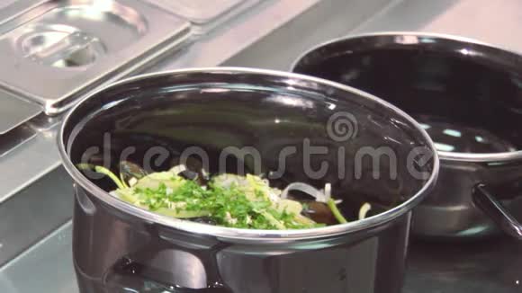 厨师在平底锅中从塑料容器中加入罗勒里面有贻贝桌子上有绿色植物餐厅视频的预览图
