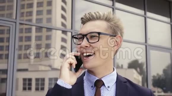 年轻英俊的高加索商人戴着眼镜在办公楼前用手机说话男性行政主管视频的预览图