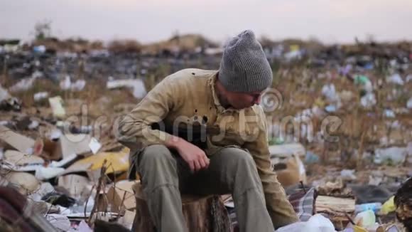 肮脏的流浪汉坐在垃圾桶的树桩上视频的预览图