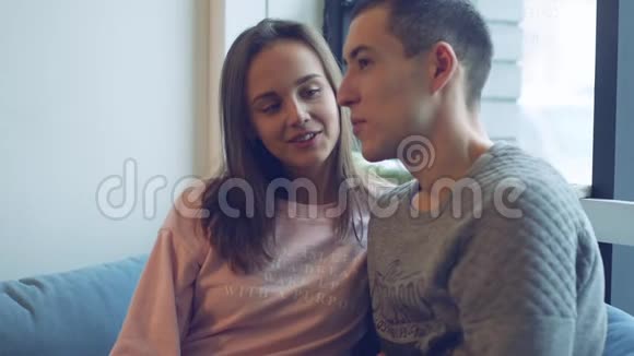 漂亮的年轻夫妇带着愉快的谈话笑坐在窗前视频的预览图
