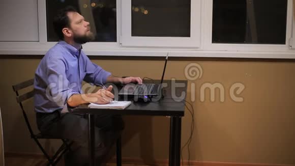 一个疲惫的商人晚上工作到很晚办公室里拿着一台笔记本电脑写了一份财务报告视频的预览图